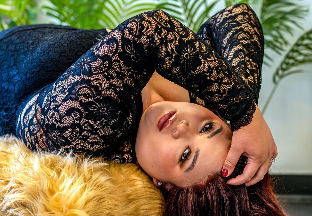 Artistic boudoir portrait with tropical plants and elegant black lace against light background.