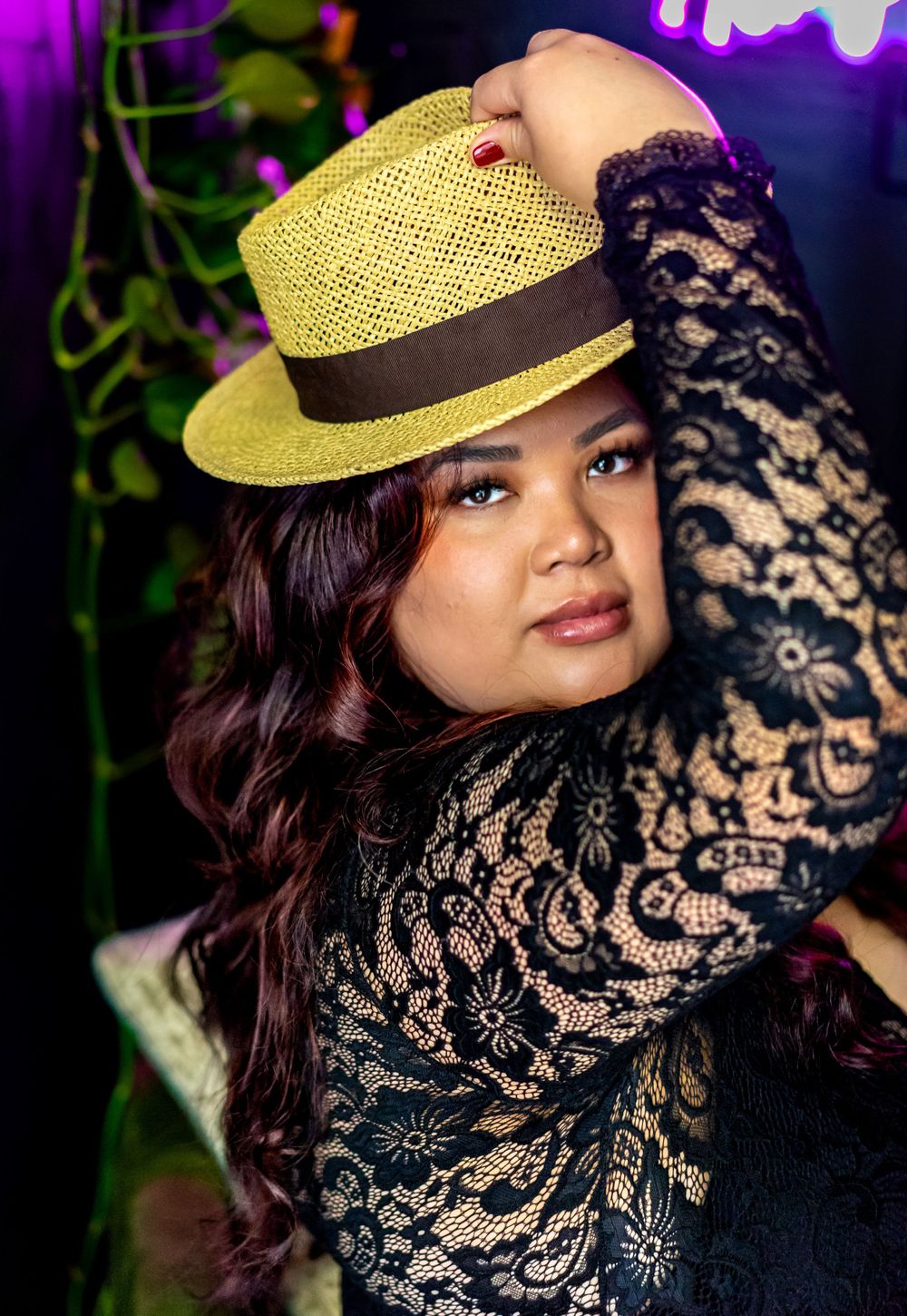 Glamour portrait with vintage straw hat and black lace against purple neon-lit background.