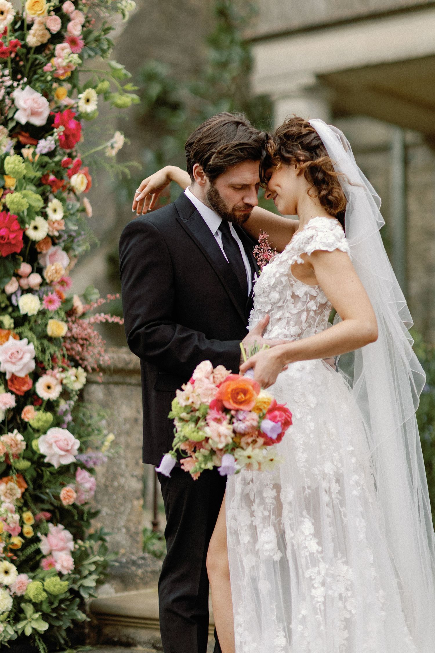 An intimate wedding moment beside a lush floral arch installation.
