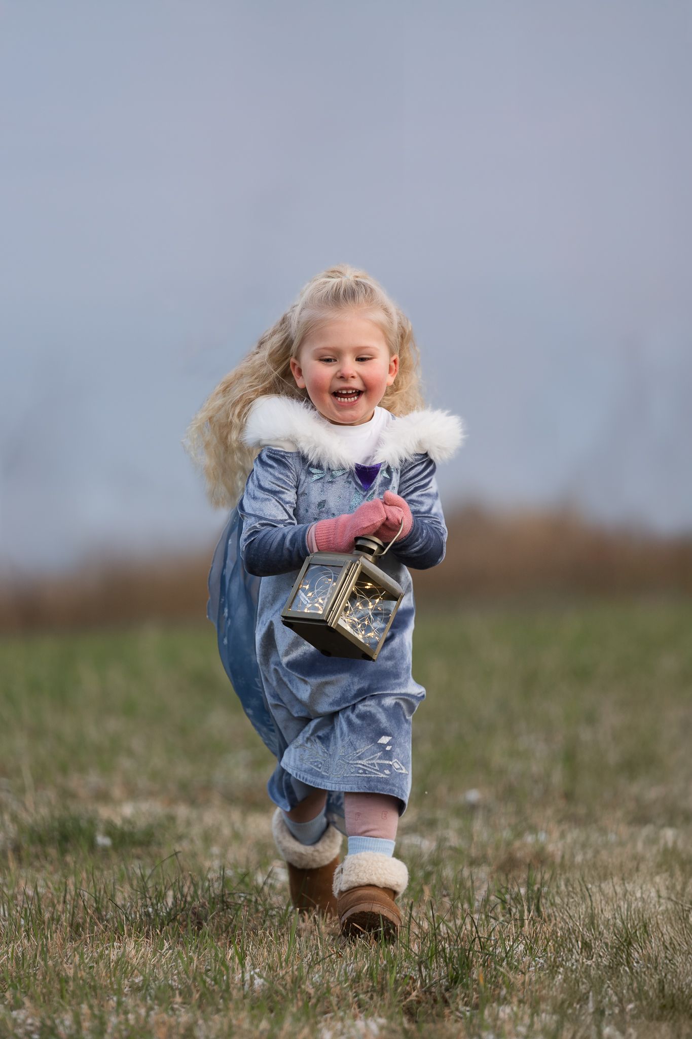 A child in denim runs and plays joyfully across a grassy field.
