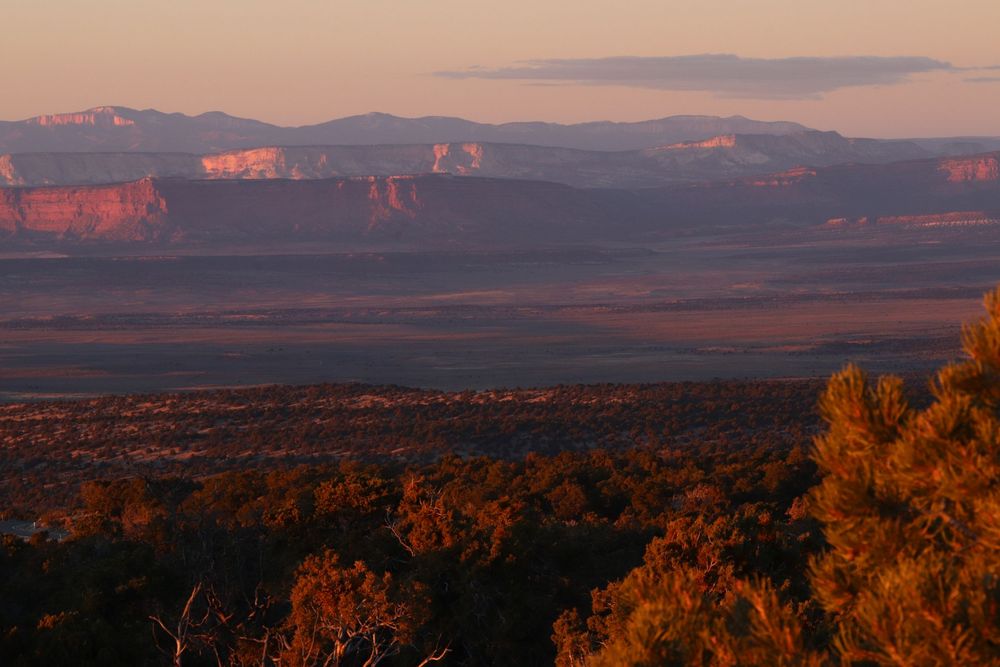 Panoramic sunset view over vast red rock canyon landscape with distant mesas bathed in warm golden light.