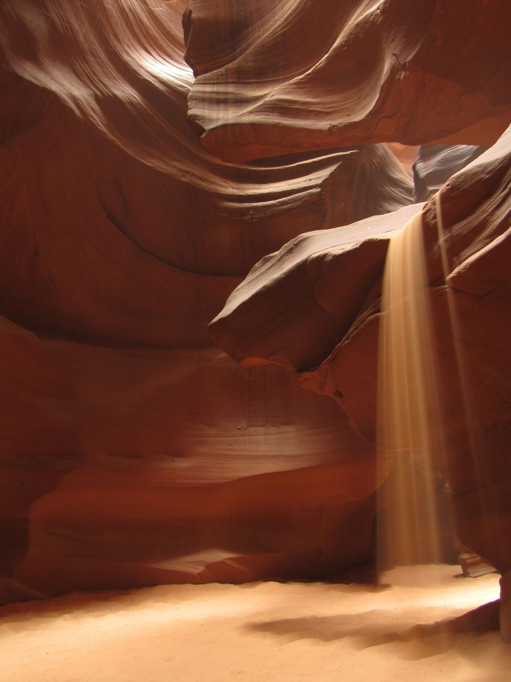 Sand cascading down through a beam of light inside the glowing walls of Antelope Canyon.