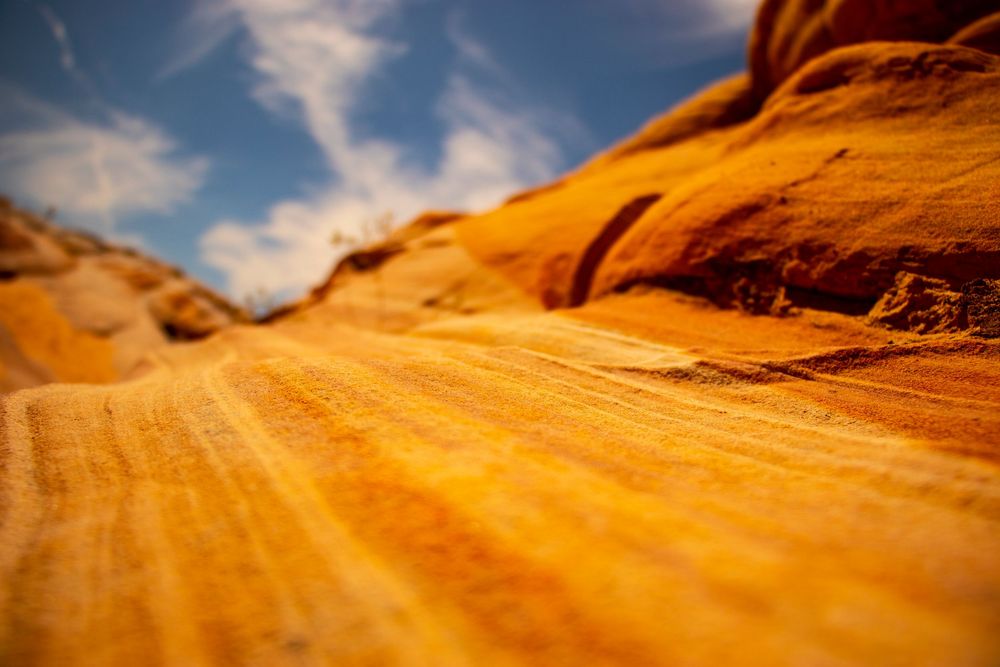 Close-up of vibrant orange layered sandstone rock surface with blue sky and clouds above.