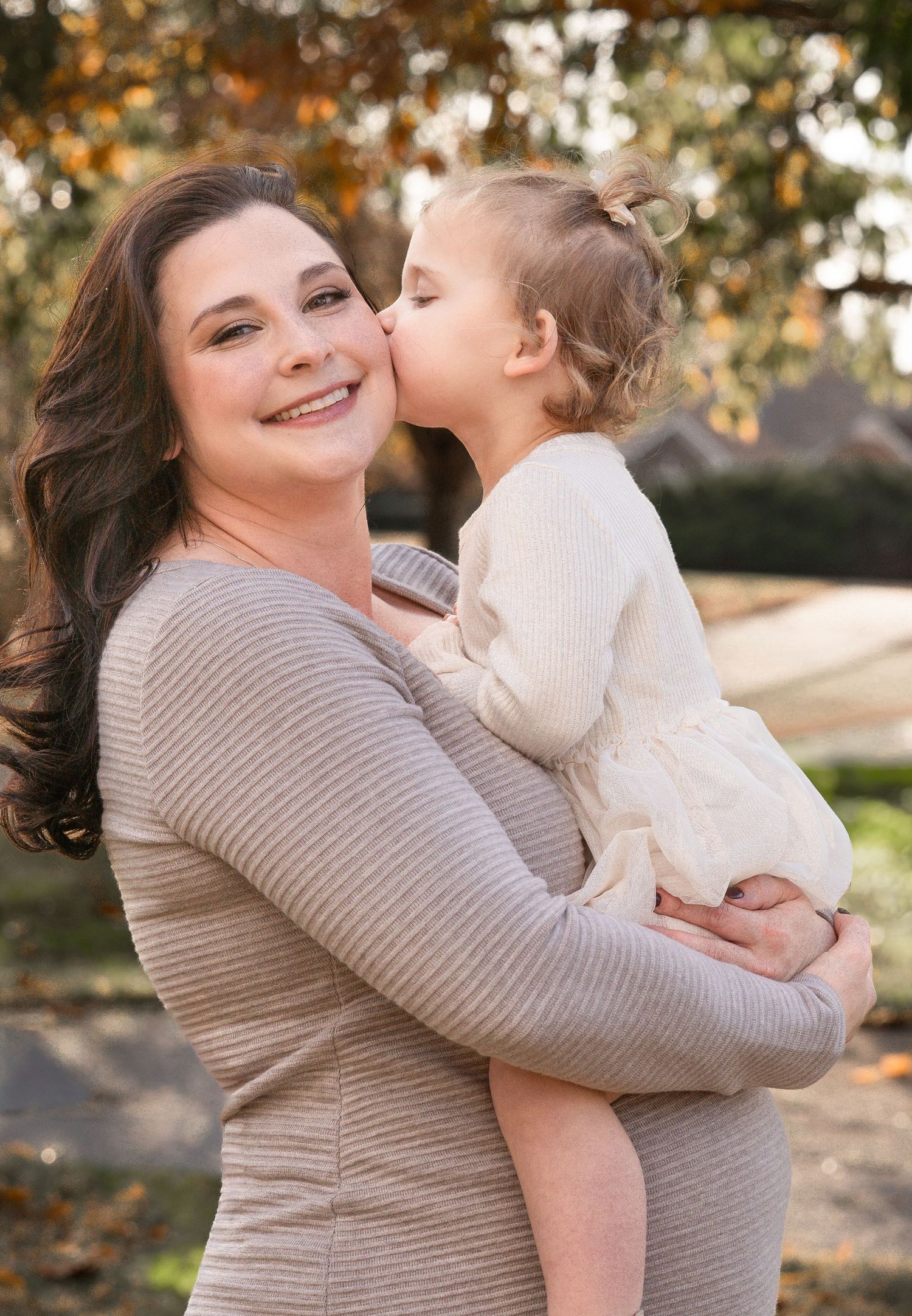A parent and child share joyful embraces in an outdoor autumn setting with golden sunlight filtering through trees.