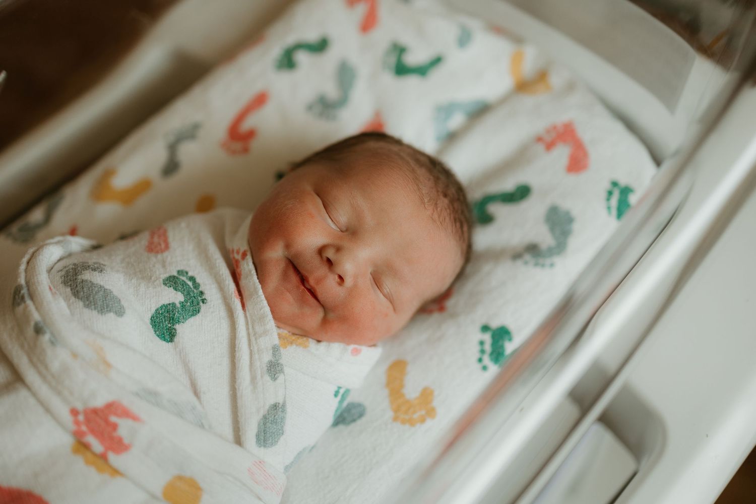 Sleeping newborn swaddled in white blanket with colorful dinosaur print pattern.