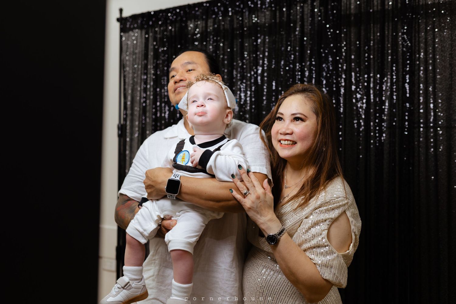Three people pose together against a black sequin backdrop during a celebratory event.