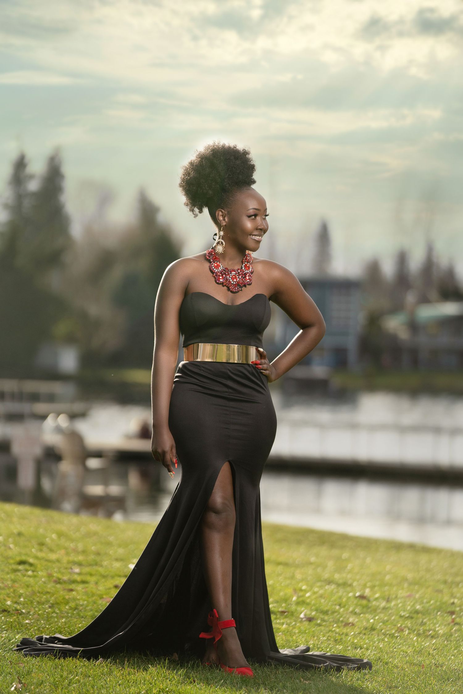 Elegant black evening gown with gold belt photographed at waterfront.