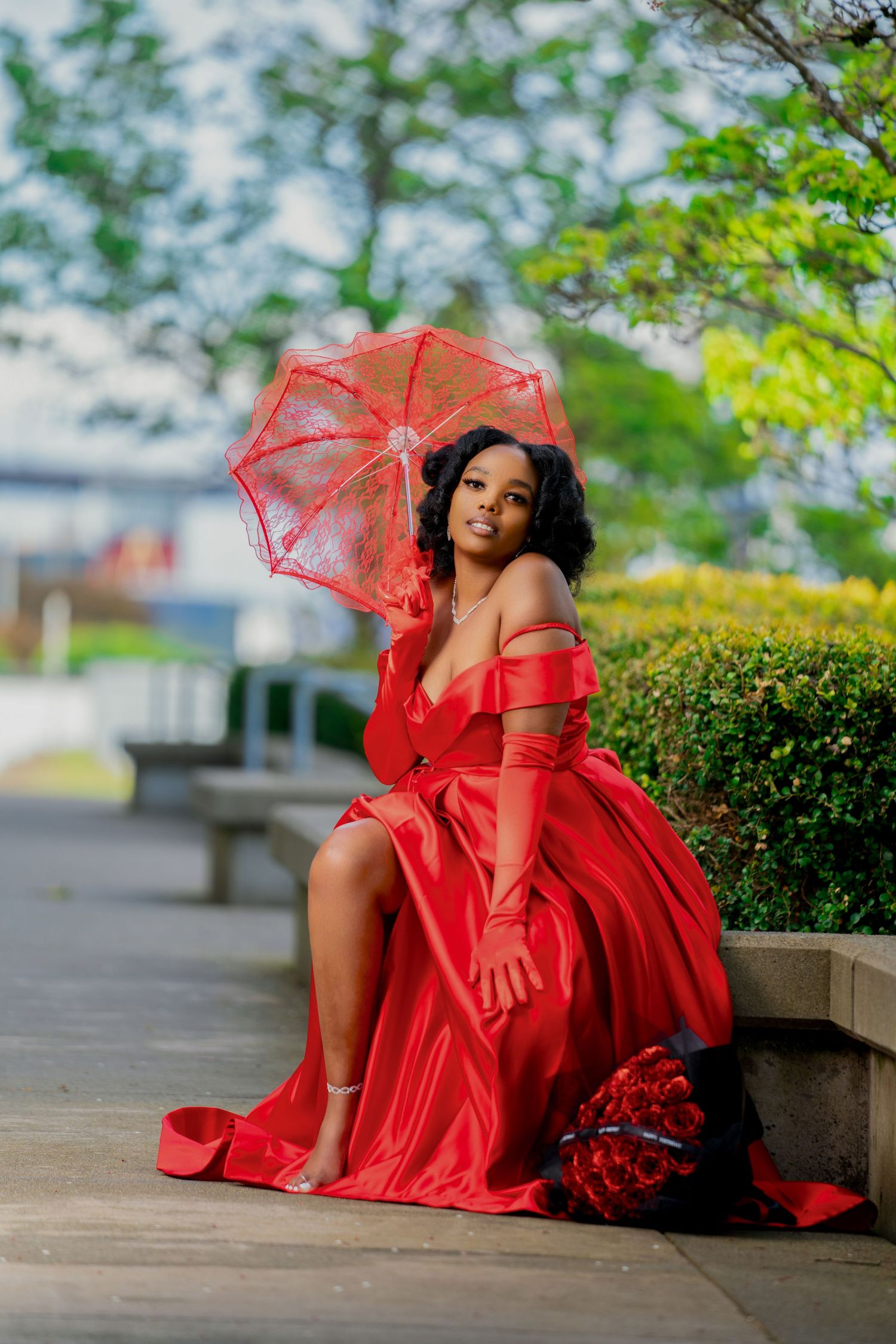 Elegant red dress and parasol captured in garden setting.