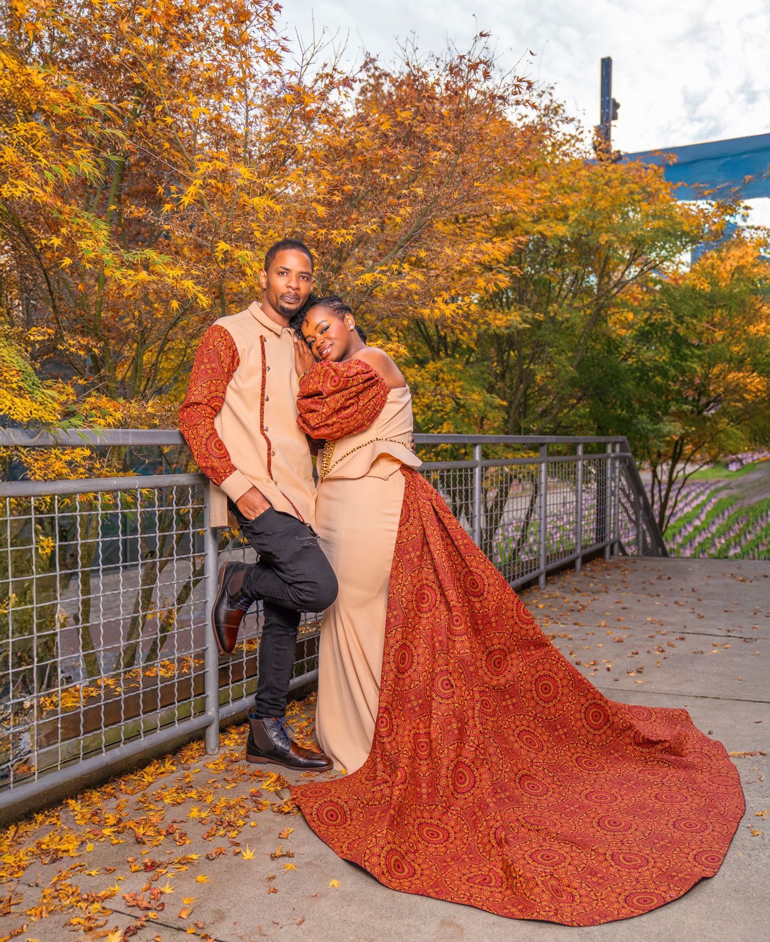 A couple poses romantically on fallen autumn leaves with a flowing red dress creating dramatic movement in the scene.