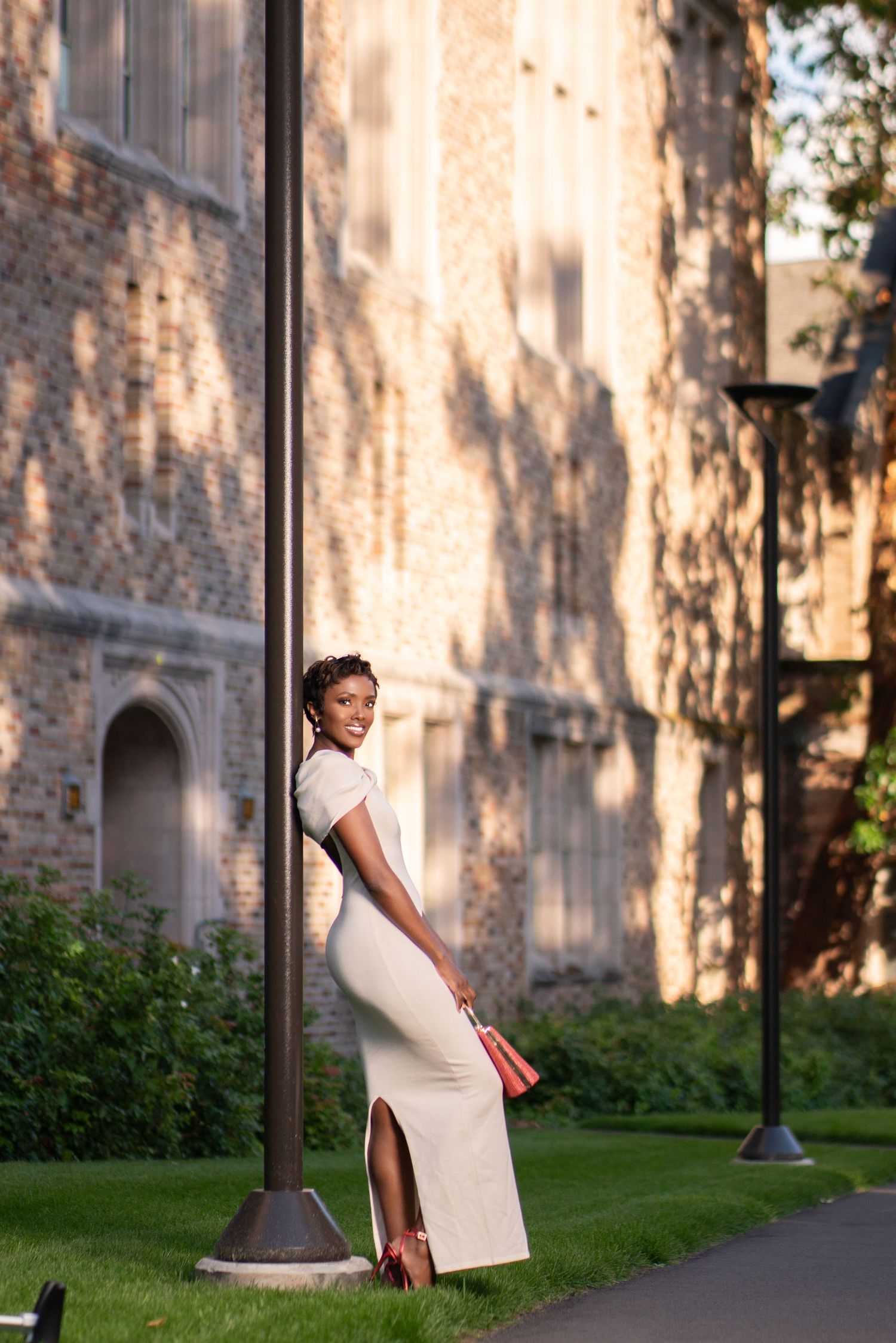 Elegant white dress portrait against historic stone building in evening light.