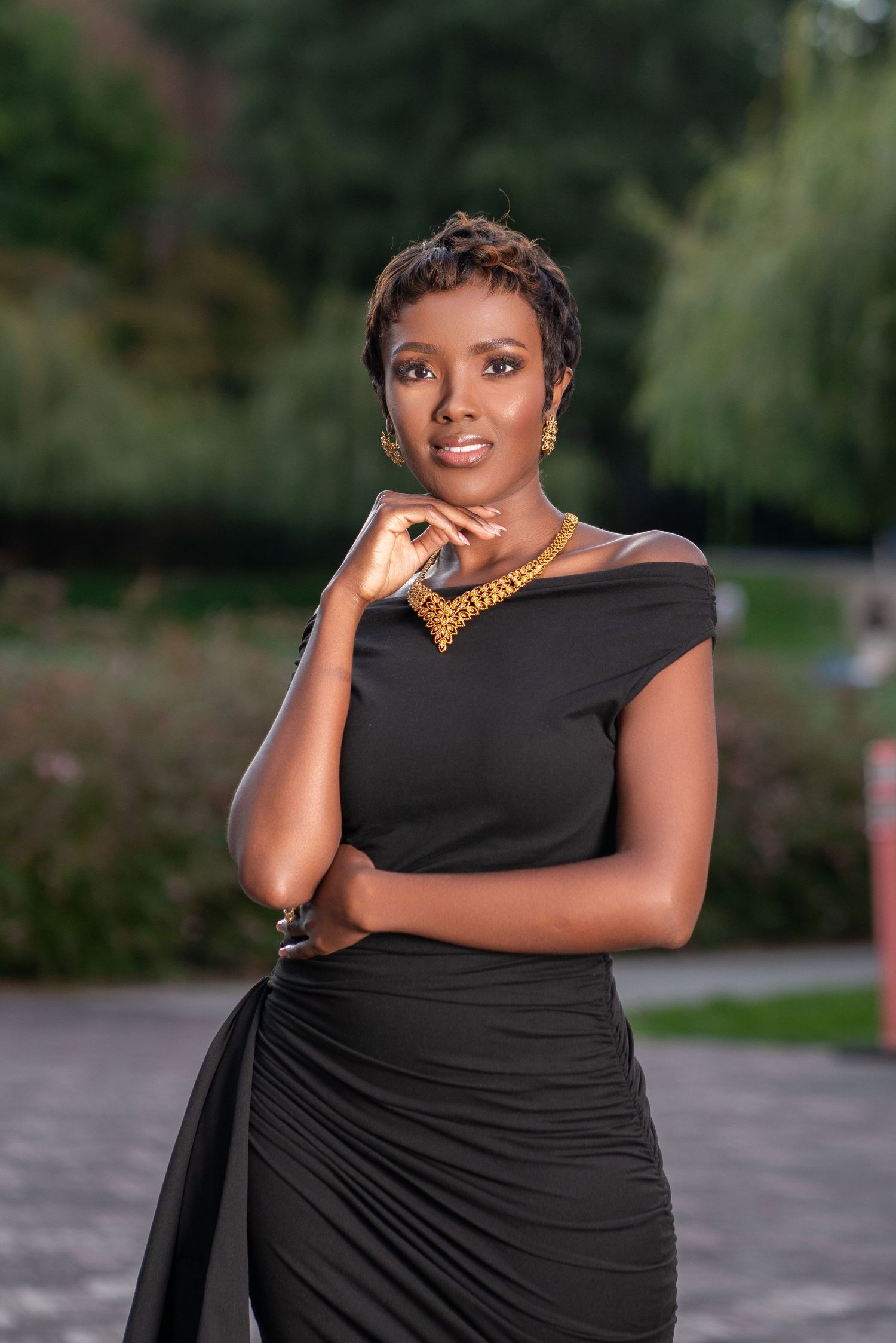 Sophisticated portrait in black dress with gold necklace in garden setting.