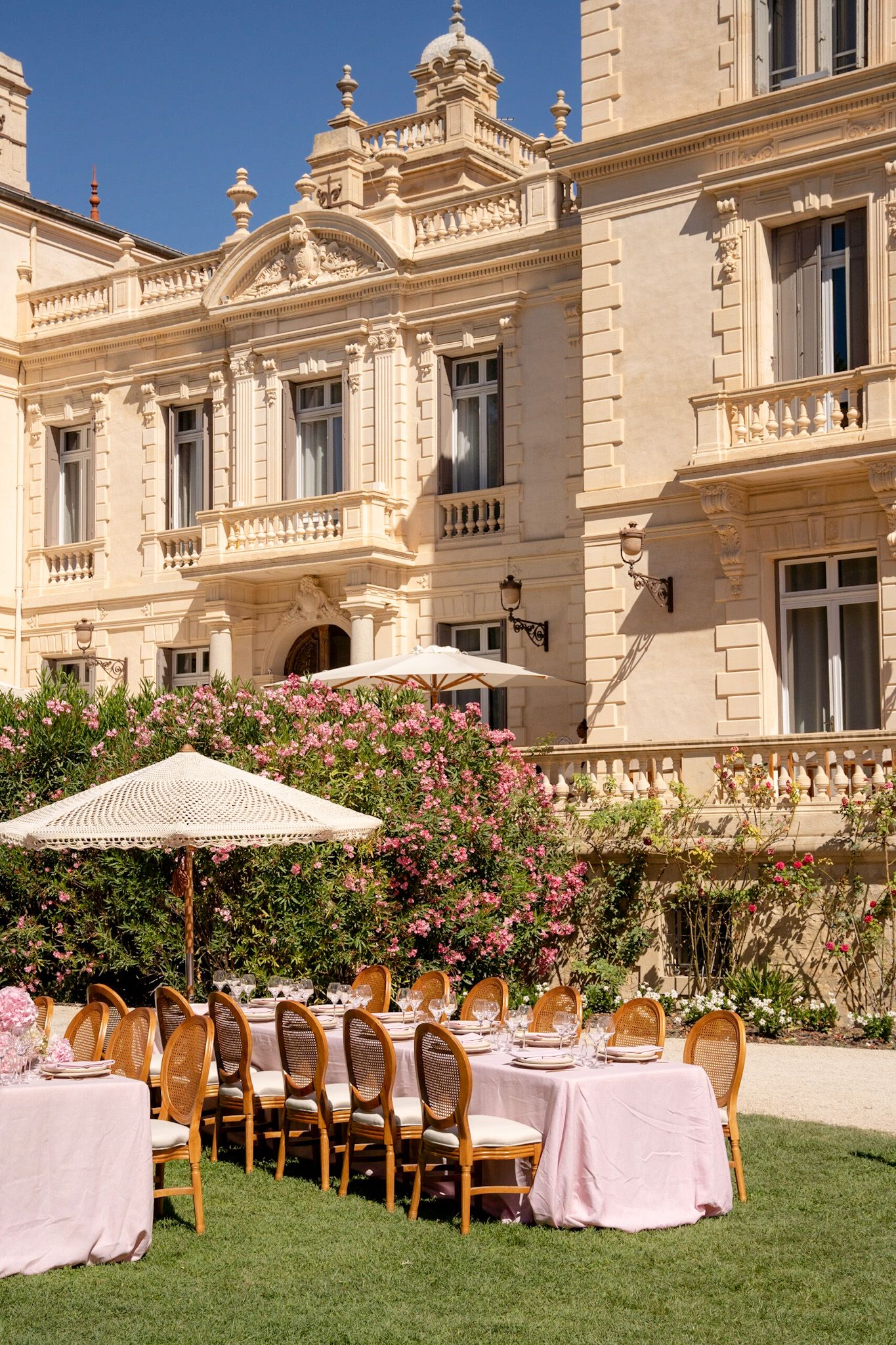 Elegant outdoor wedding reception setup with long tables and umbrellas against a grand historic mansion facade.