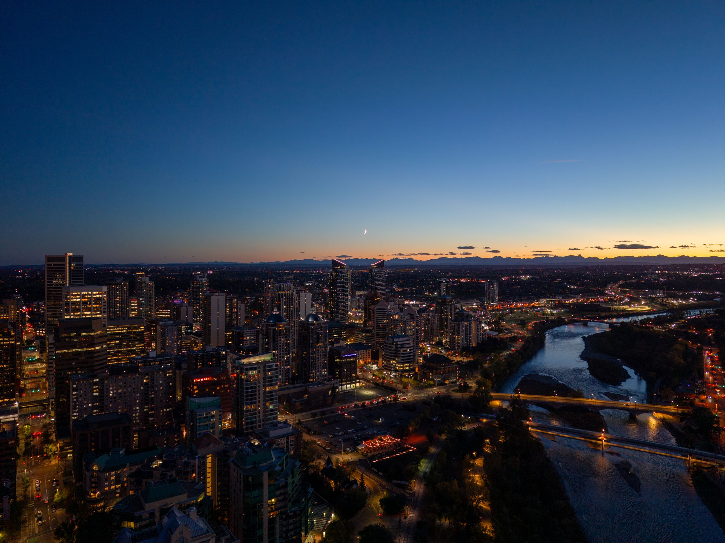 Aerial view of Pittsburgh's illuminated skyline and rivers at dusk with glowing city lights reflecting on the water.