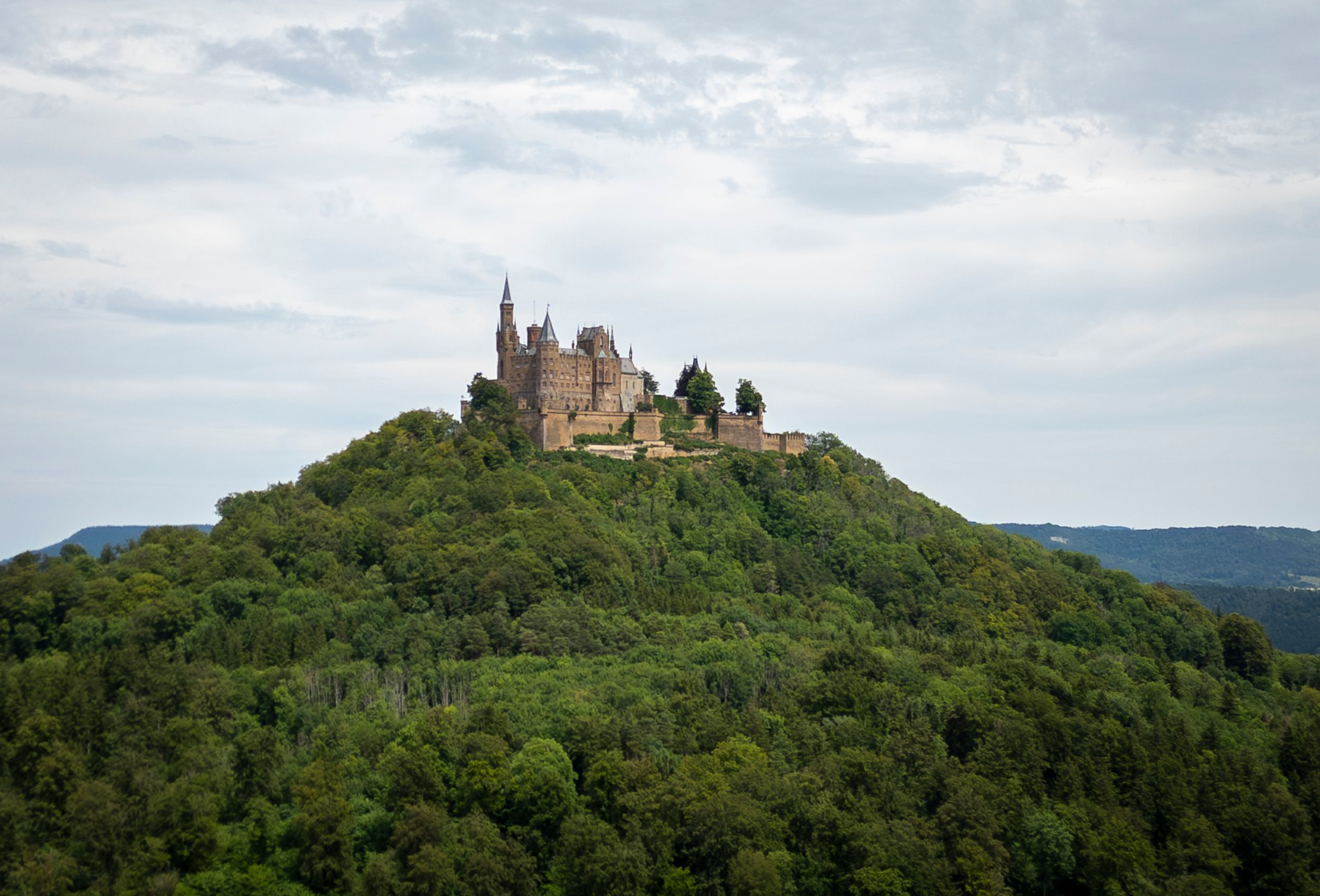 Ancient hilltop castle Hohenzollern perched atop a forested mountain in Germany against a cloudy sky.