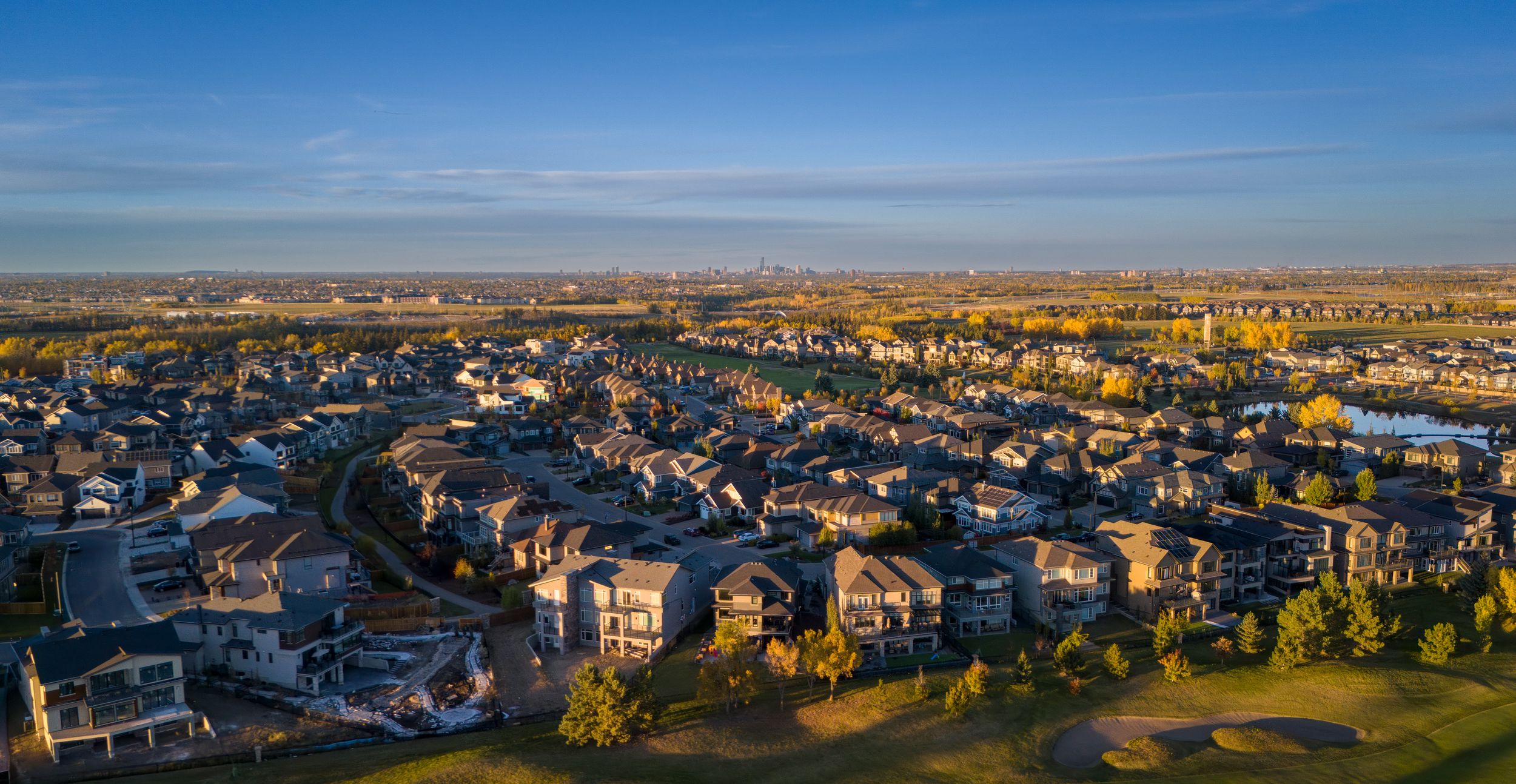 Panoramic aerial view of suburban neighborhood with modern homes under blue sky at sunset.