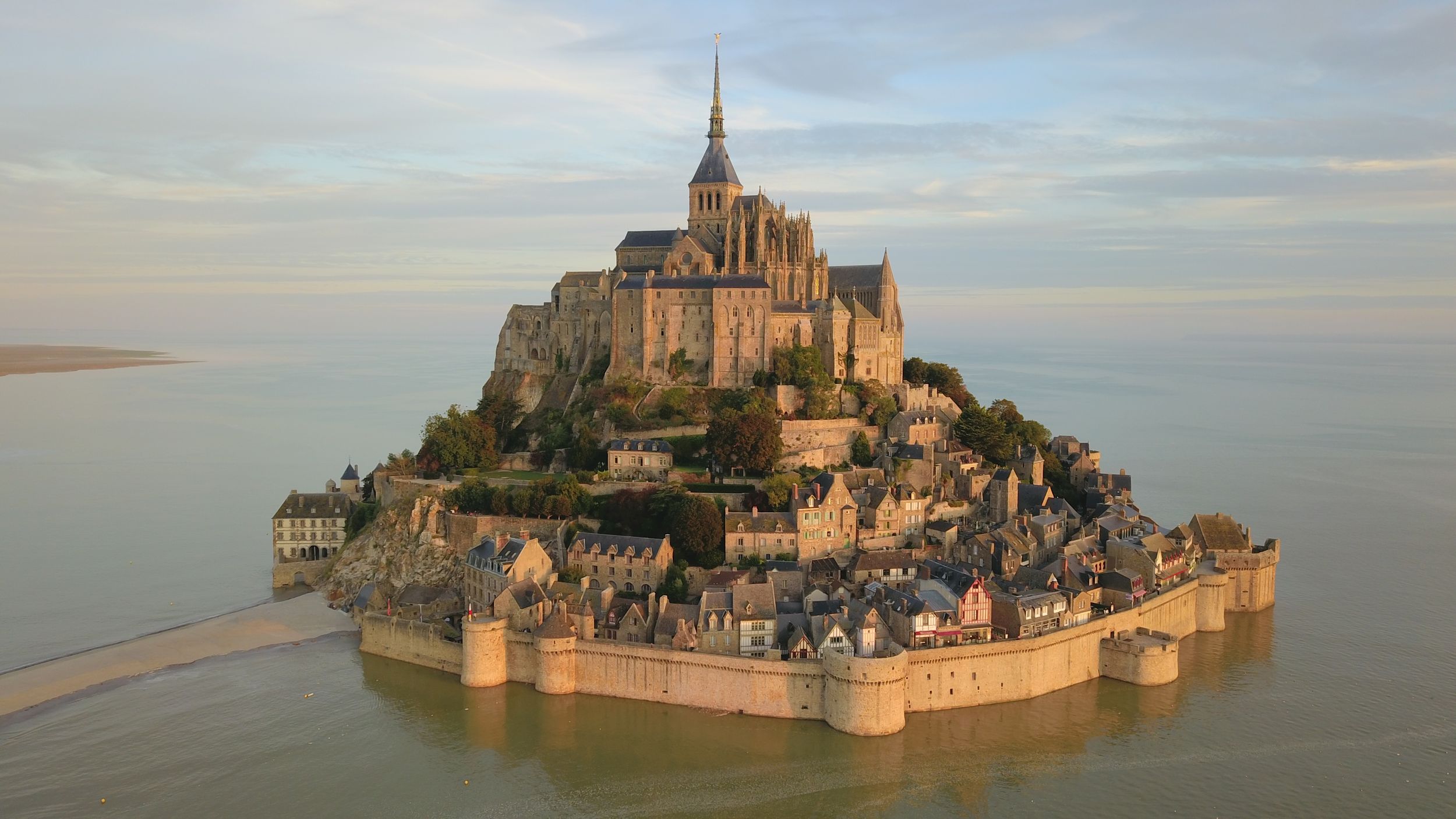 Mont Saint-Michel island fortress rises majestically from the misty bay at sunset in Normandy, France.