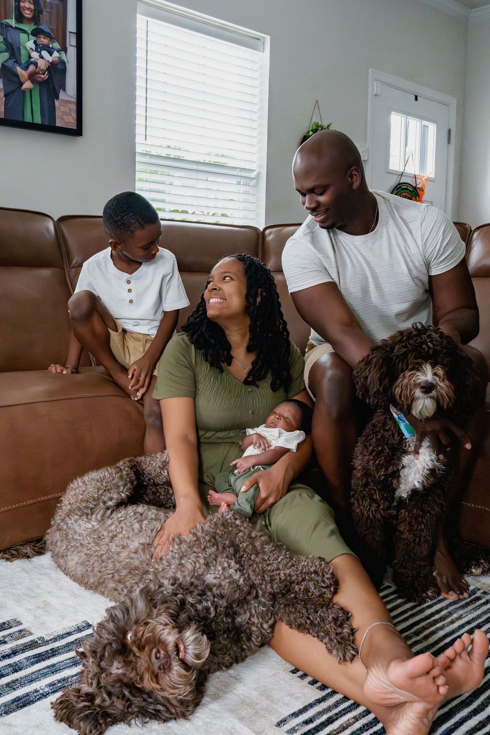 Happy Black family with newborn baby, older child, and two brown curly dogs sitting together in cozy living room, in Hanover, MD