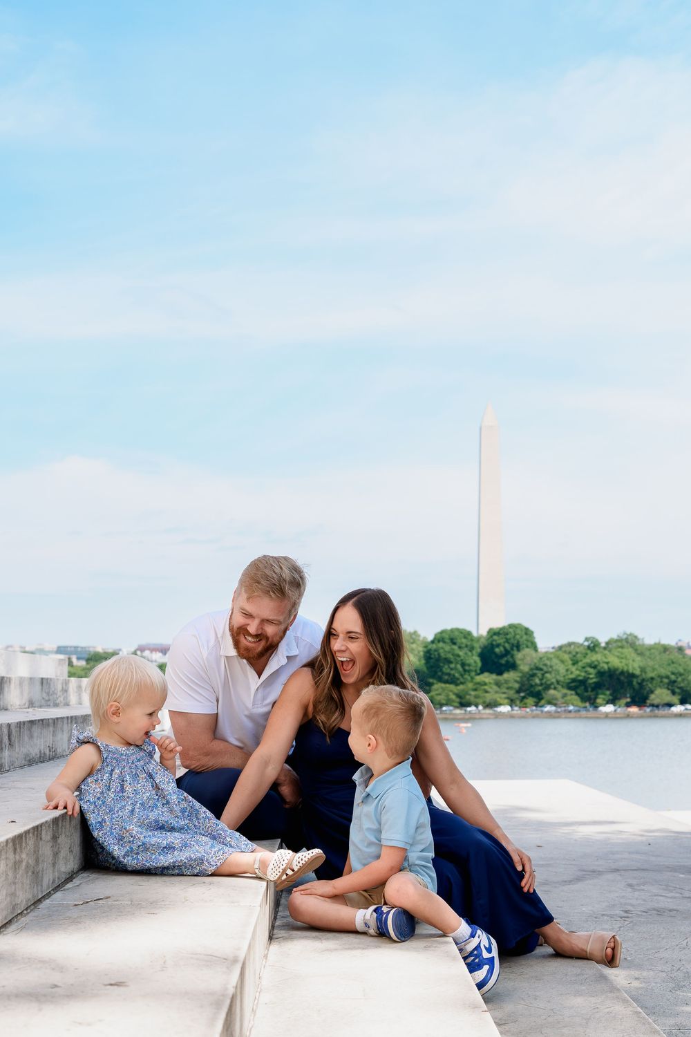 Family of four smiling and laughing together on steps near the Washington Monument and Tidal Basin in DC.