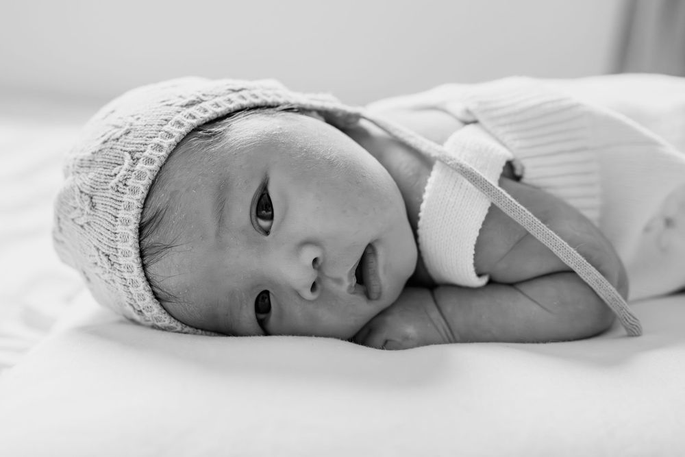 Black and white photo of a peaceful newborn baby wearing a knit bonnet, lying on a soft white blanket, in Fairfax, VA