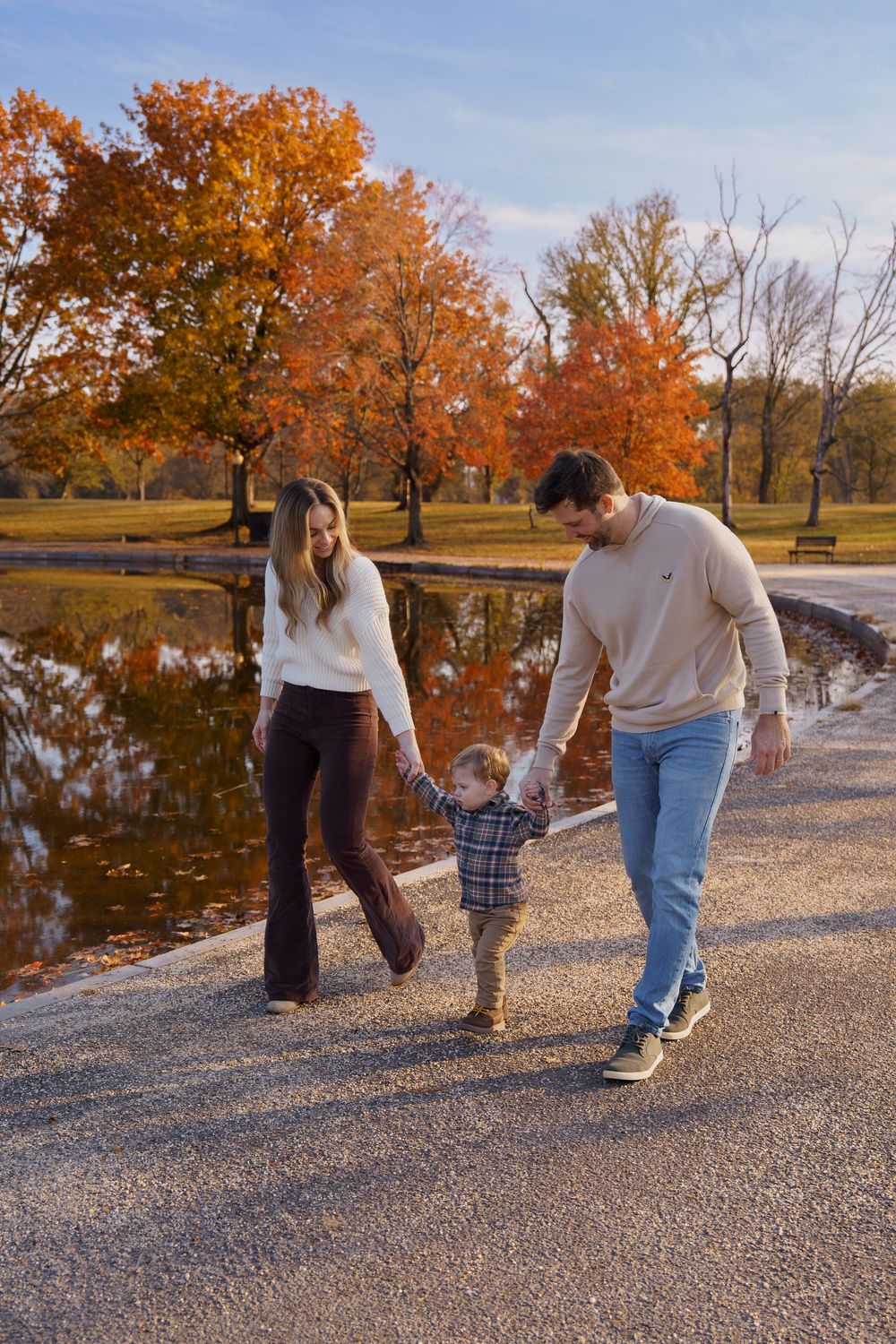 Family of three walking hand-in-hand by a pond in an autumn park with vibrant orange and red foliage, in Washington DC