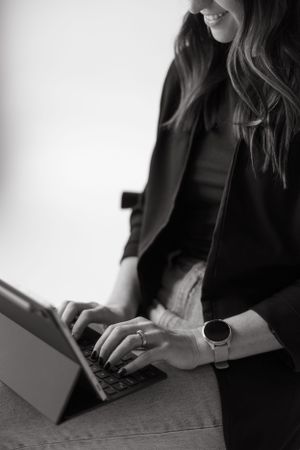 Close-up of hands typing on tablet keyboard while wearing smart watch.