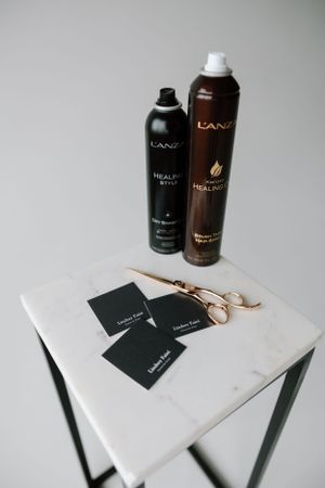 L'Anza hair products and gold scissors displayed on white marble table.