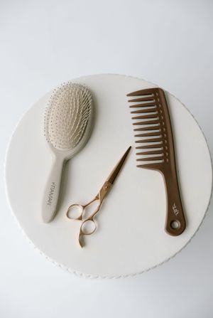 Minimalist flat lay of hair styling tools including brush, scissors and comb on white surface.