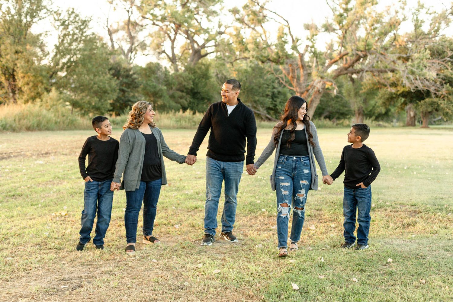 A family of five walks hand in hand through a grassy field at sunset.
