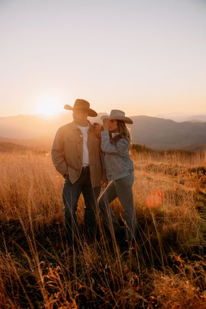 Silhouetted couple embraces in golden mountain meadow at sunset during romantic outdoor photoshoot.