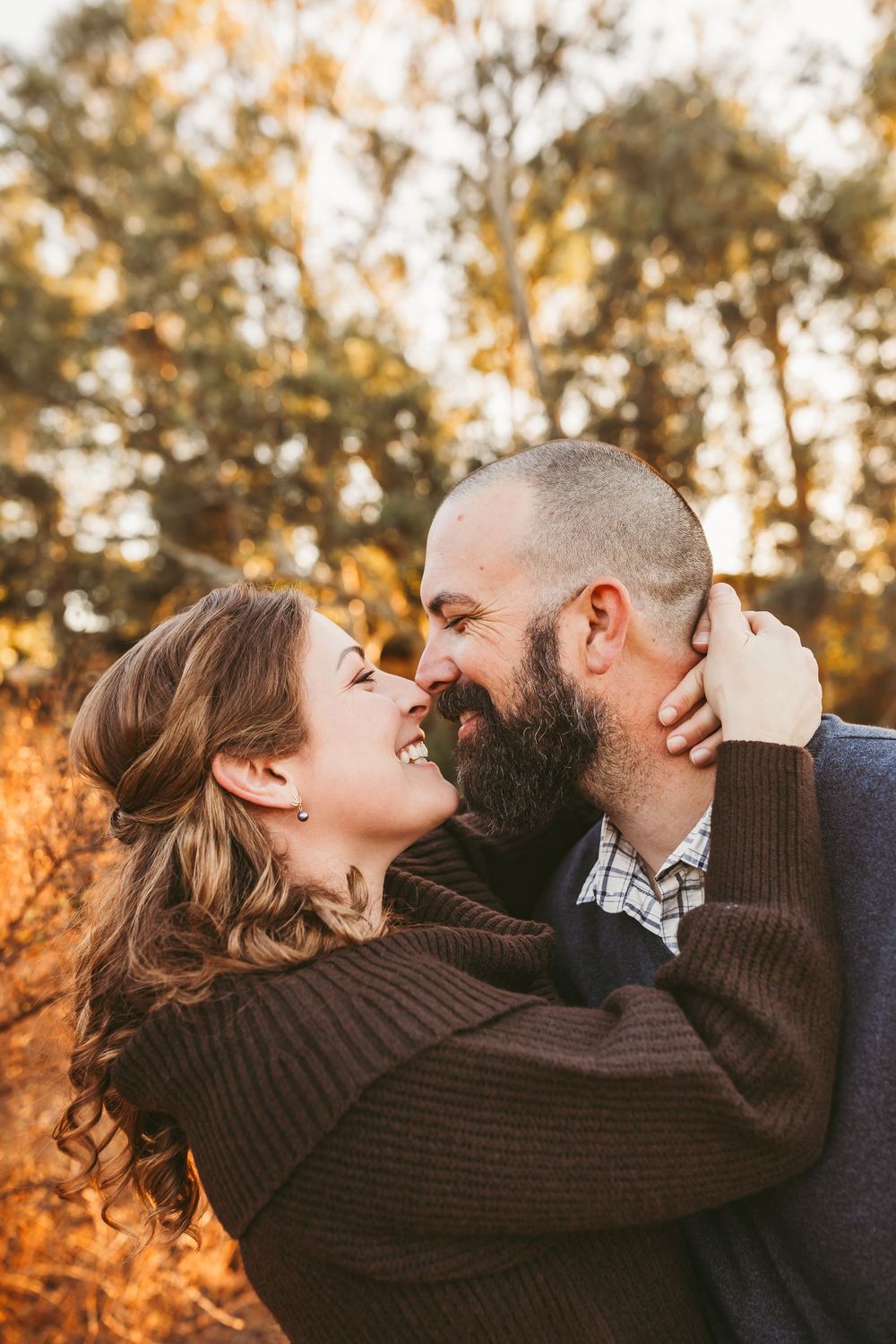Romantic couple embracing outdoors during golden hour with autumn trees in background.