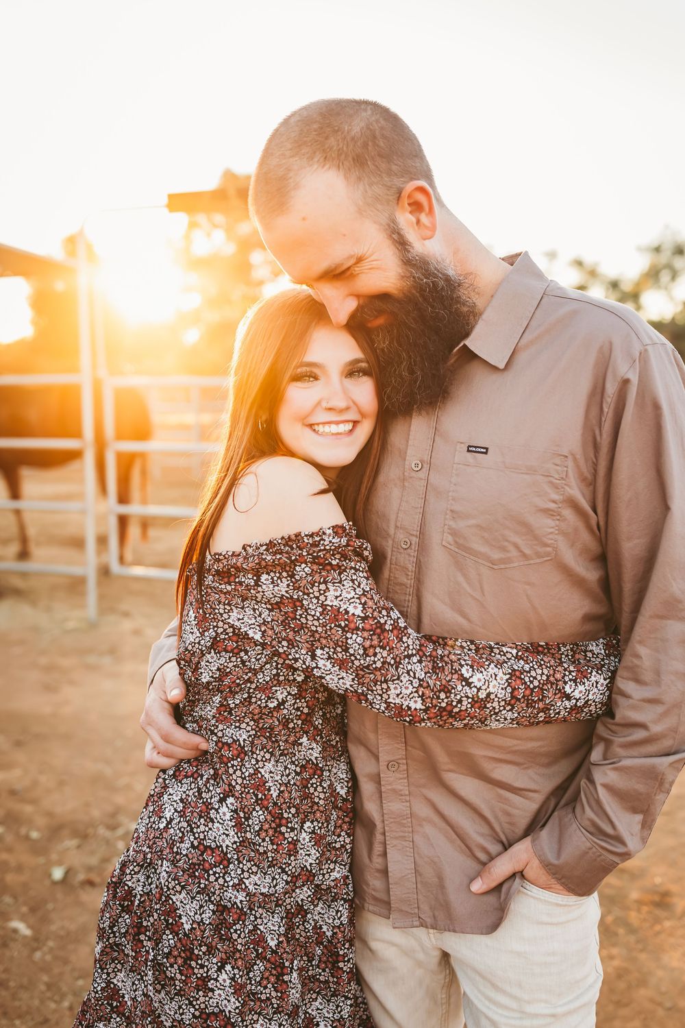 A couple embraces during golden hour in a field as sunlight creates a warm romantic glow behind them.