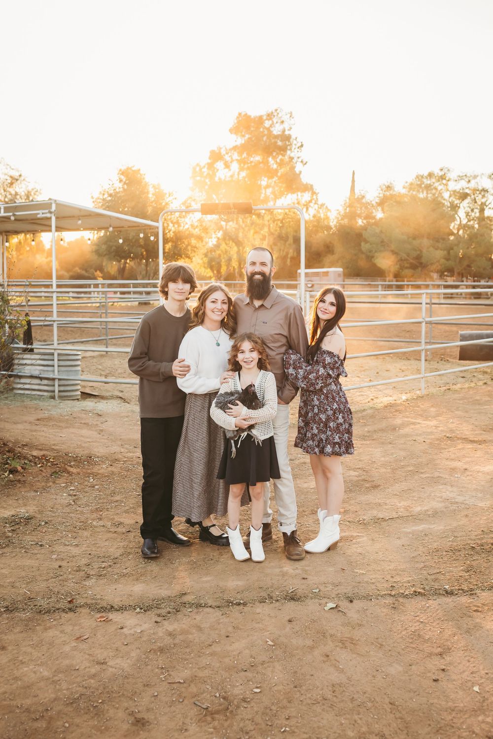 A group of people standing together at a farm corral during golden hour sunset.
