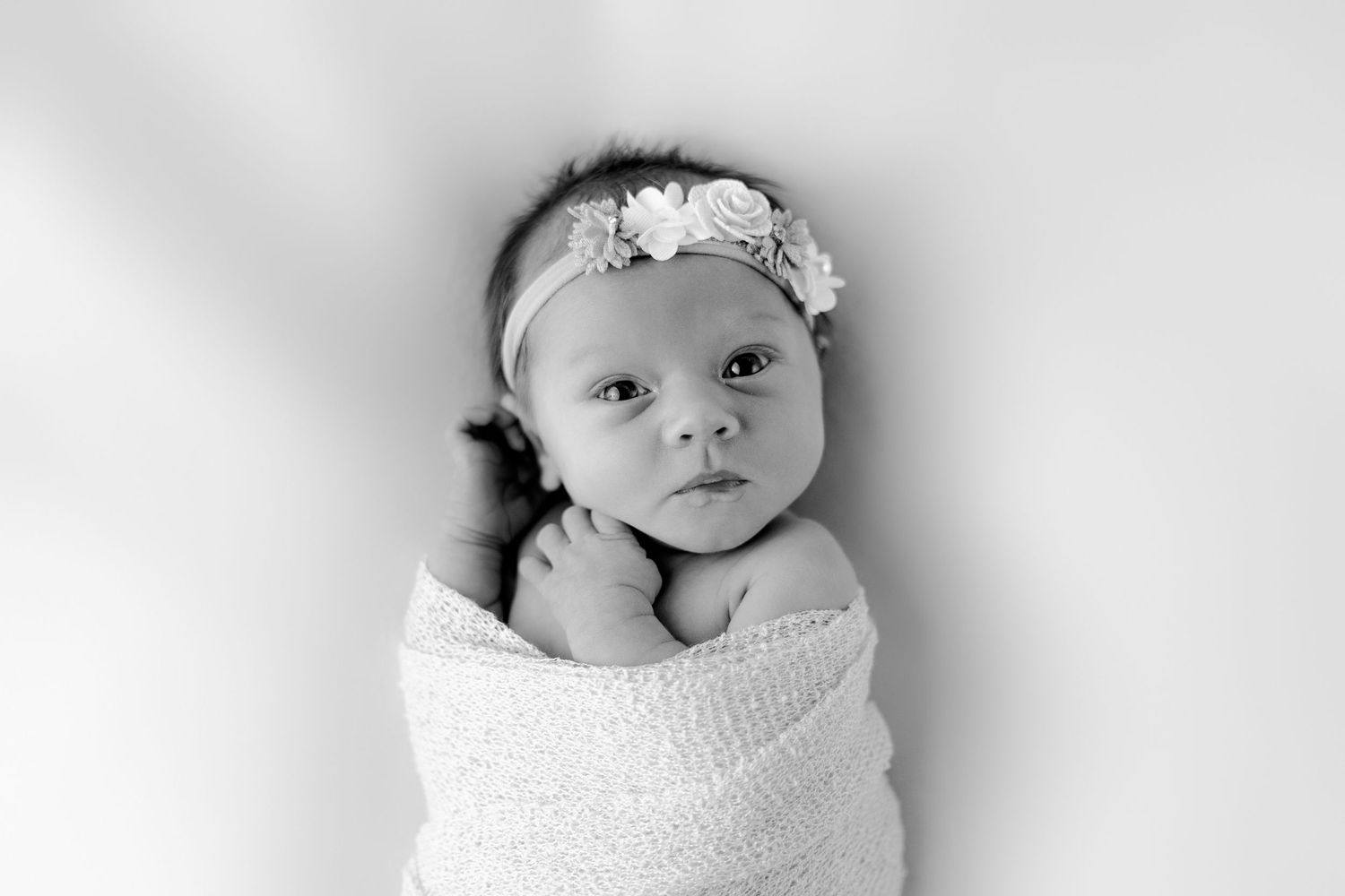 Newborn baby wrapped in white swaddle wearing delicate floral headband.