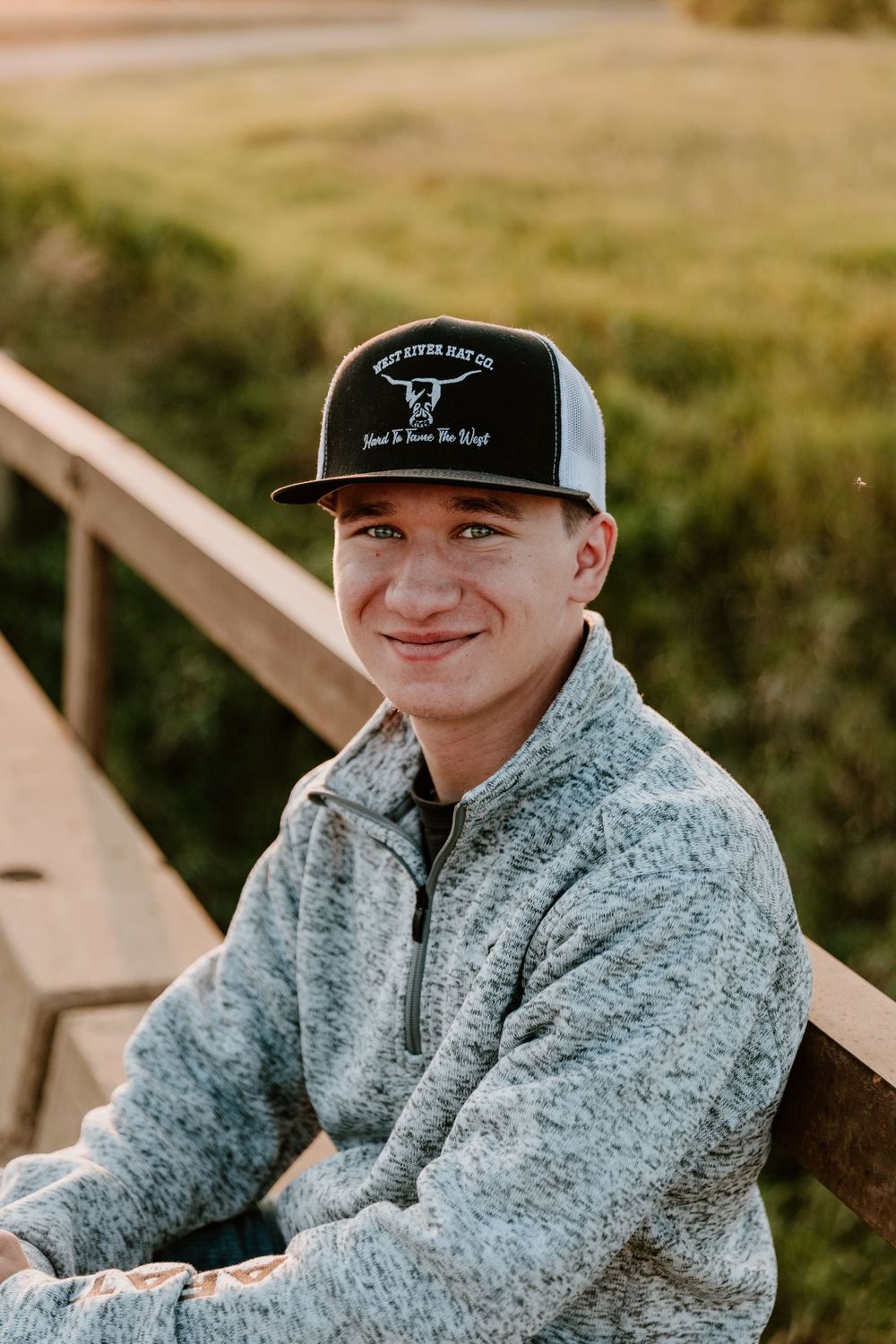 Young person in a gray fleece and baseball cap sitting outdoors on wooden steps in natural lighting.