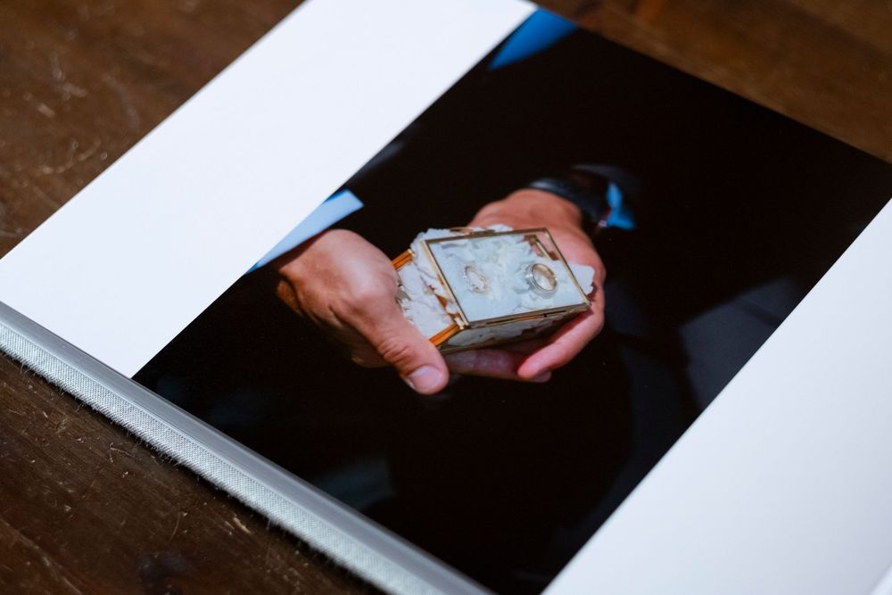 Hands holding an old weathered photograph in a photo album against a dark background.