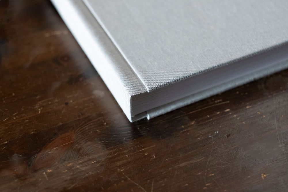 Close-up view of a white hardcover book corner resting on a dark wooden surface.