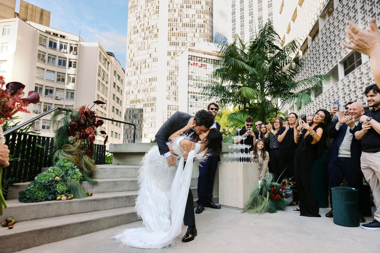 Newlyweds celebrating under palm trees with guests applauding.