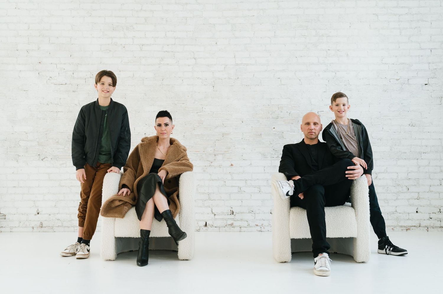 Four people in casual attire sit and stand against a white brick wall in a minimalist indoor setting.