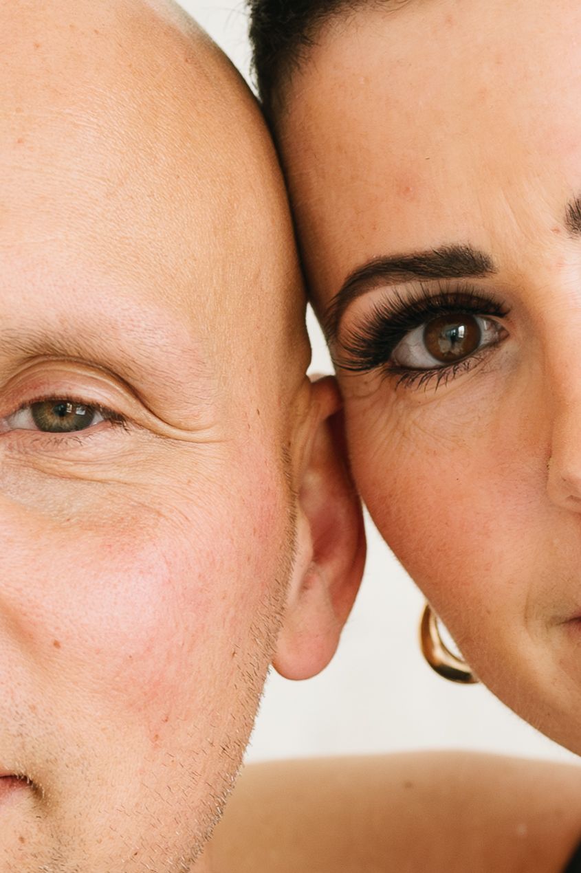 Close up intimate portrait of two people with faces touching against light background.
