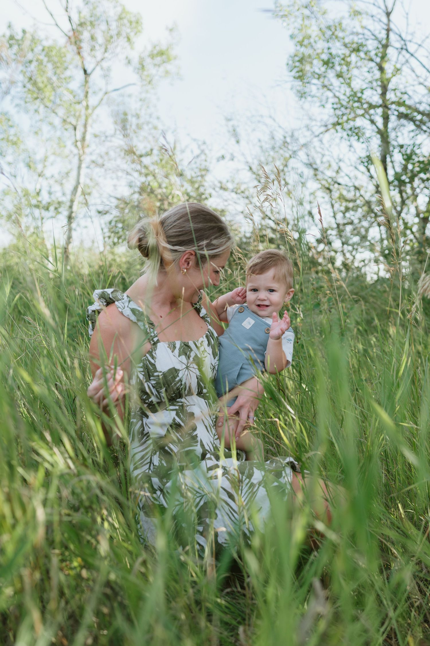 Parent and child in floral dress surrounded by tall green grass.
