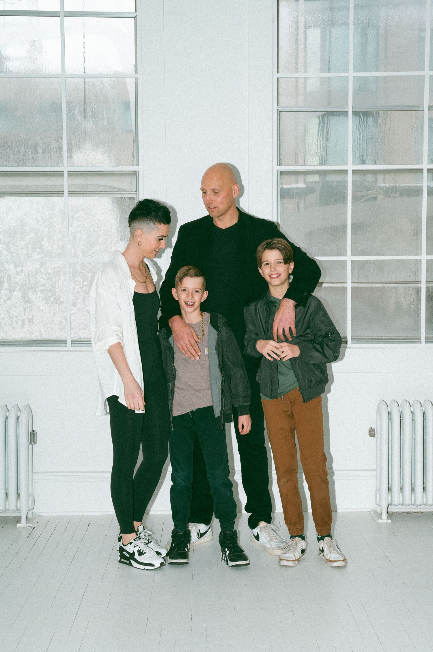 A group of four people in casual attire standing together in a bright white room with large windows and radiators.