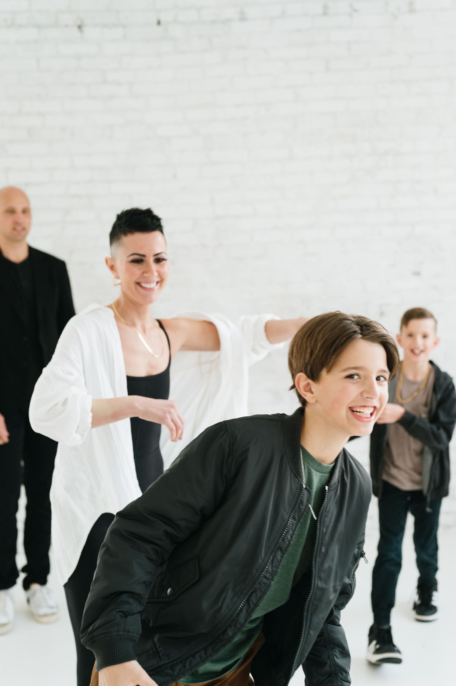 A group of dancers in casual attire rehearsing moves together in a bright white studio space.