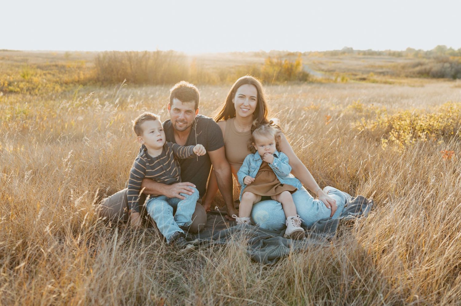 A warm family portrait taken in a golden field of tall grass during sunset.