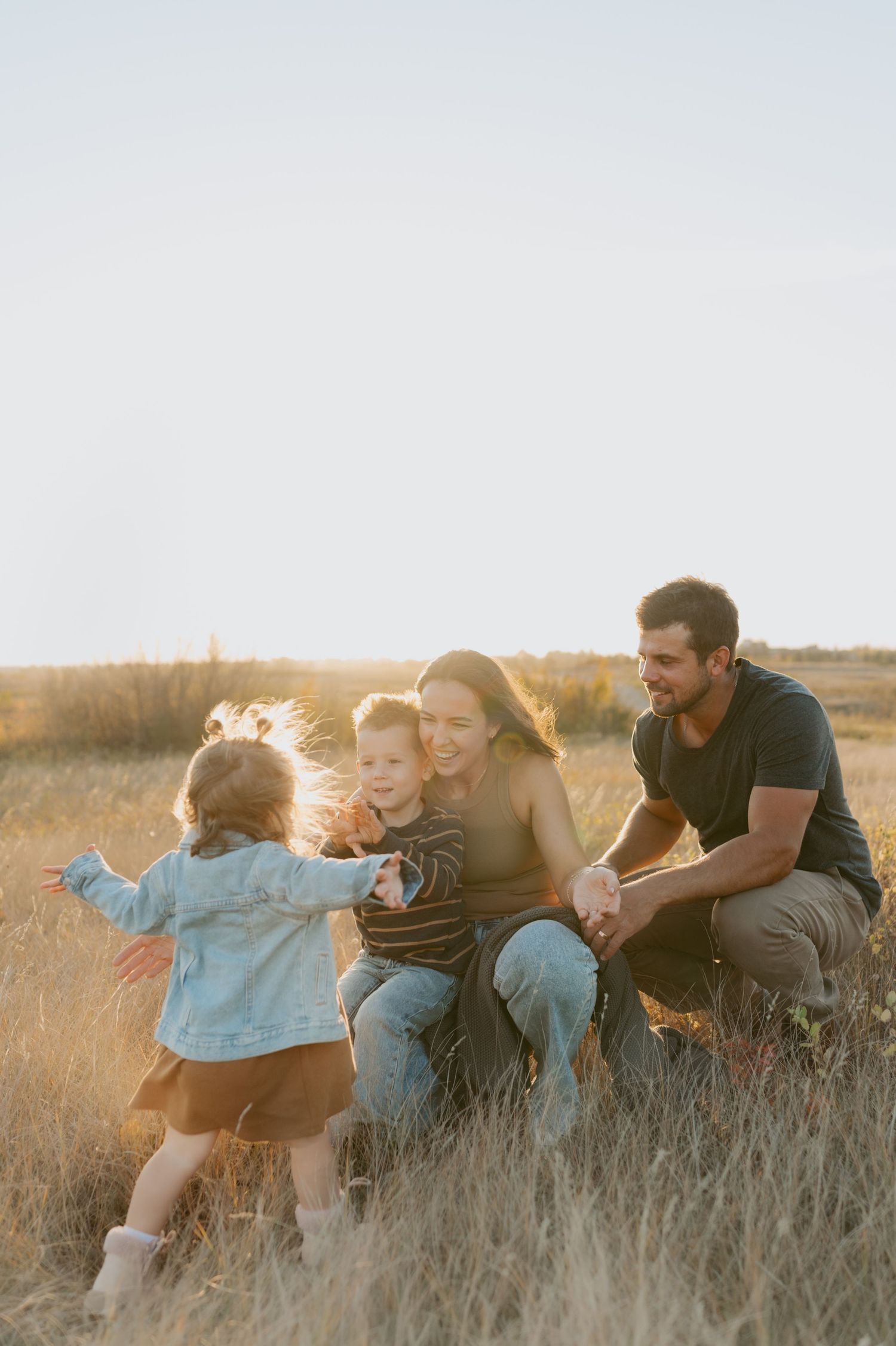 Family enjoying a candid moment together while sitting in tall grass during golden hour.