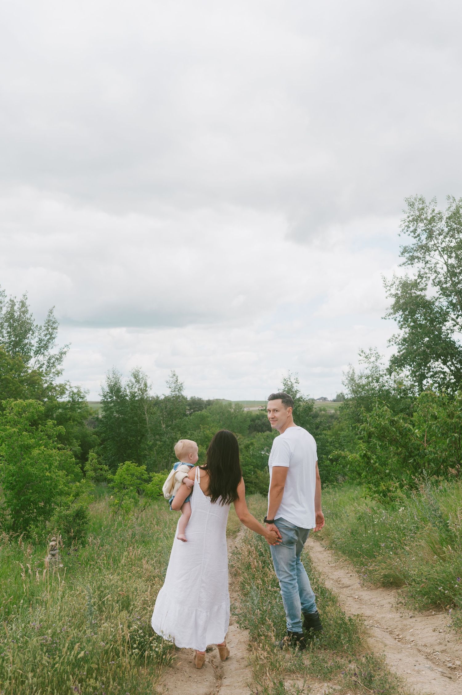 Family walking together on rural path under cloudy sky.