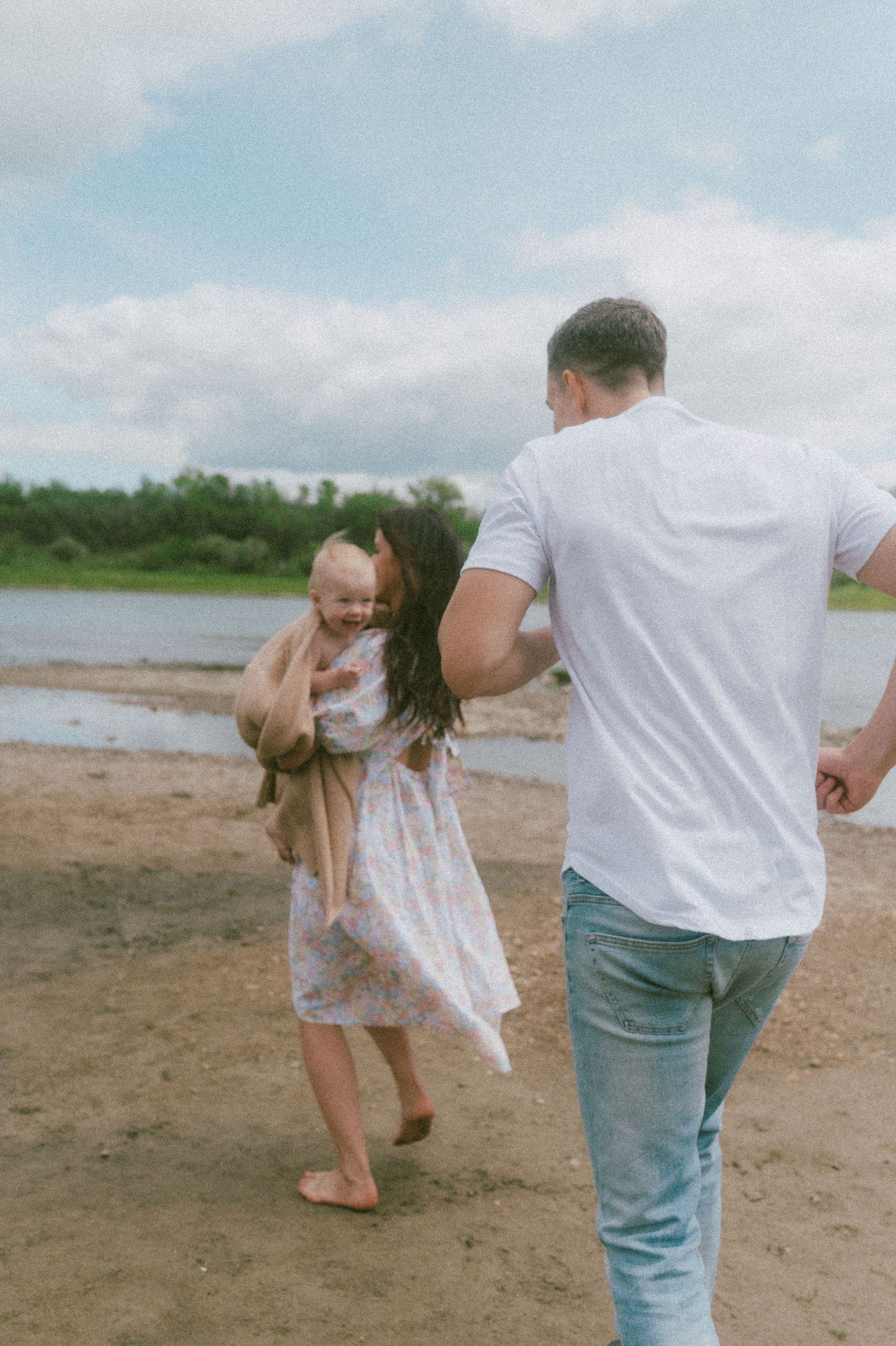 A family enjoying a playful moment together on a beach near a lake.