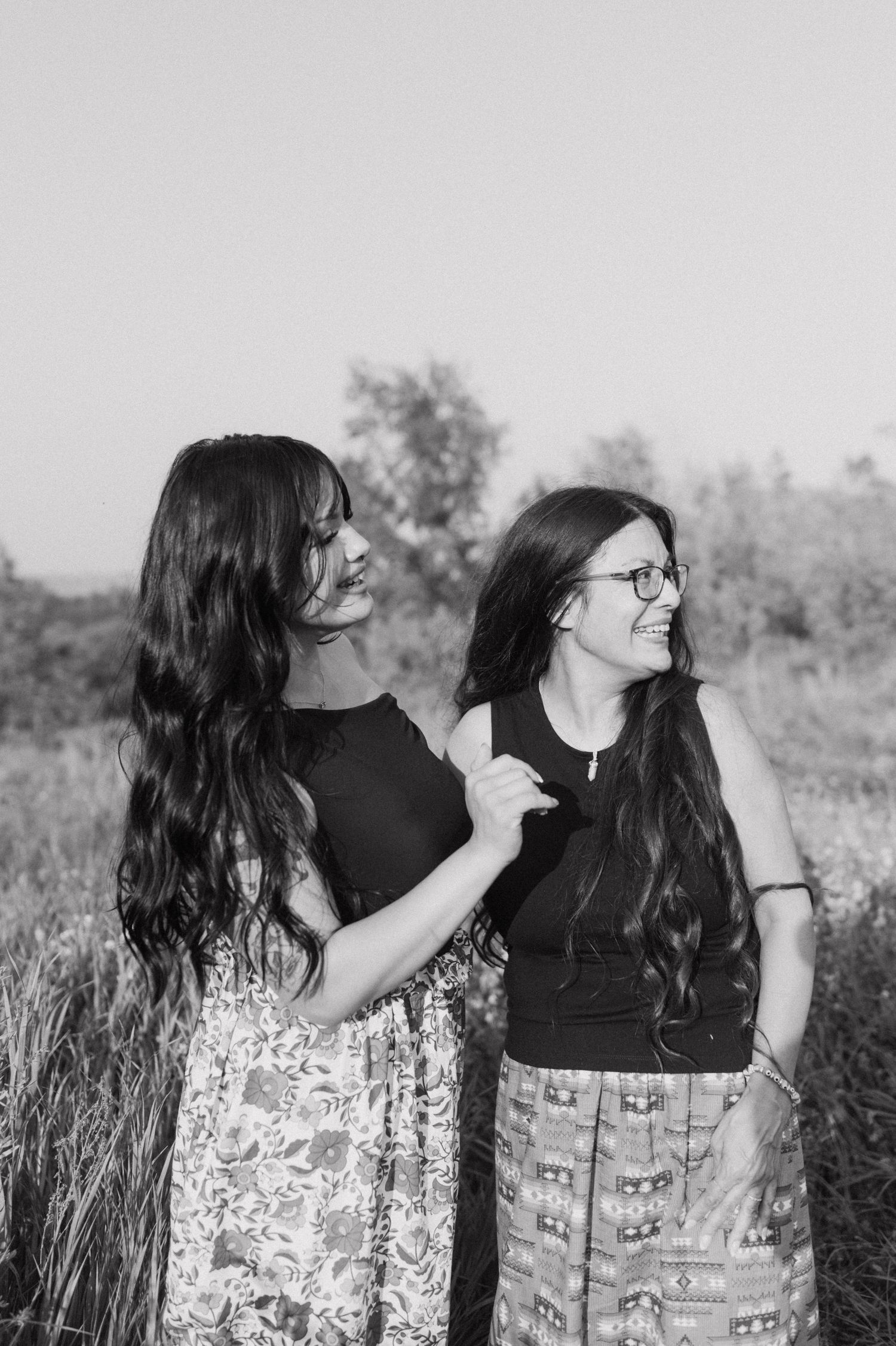 Two women in casual attire sharing a joyful moment in a field.