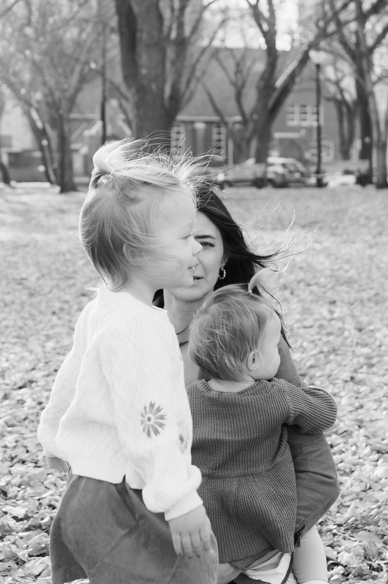 Black and white photo of family sharing a tender moment among fallen leaves.