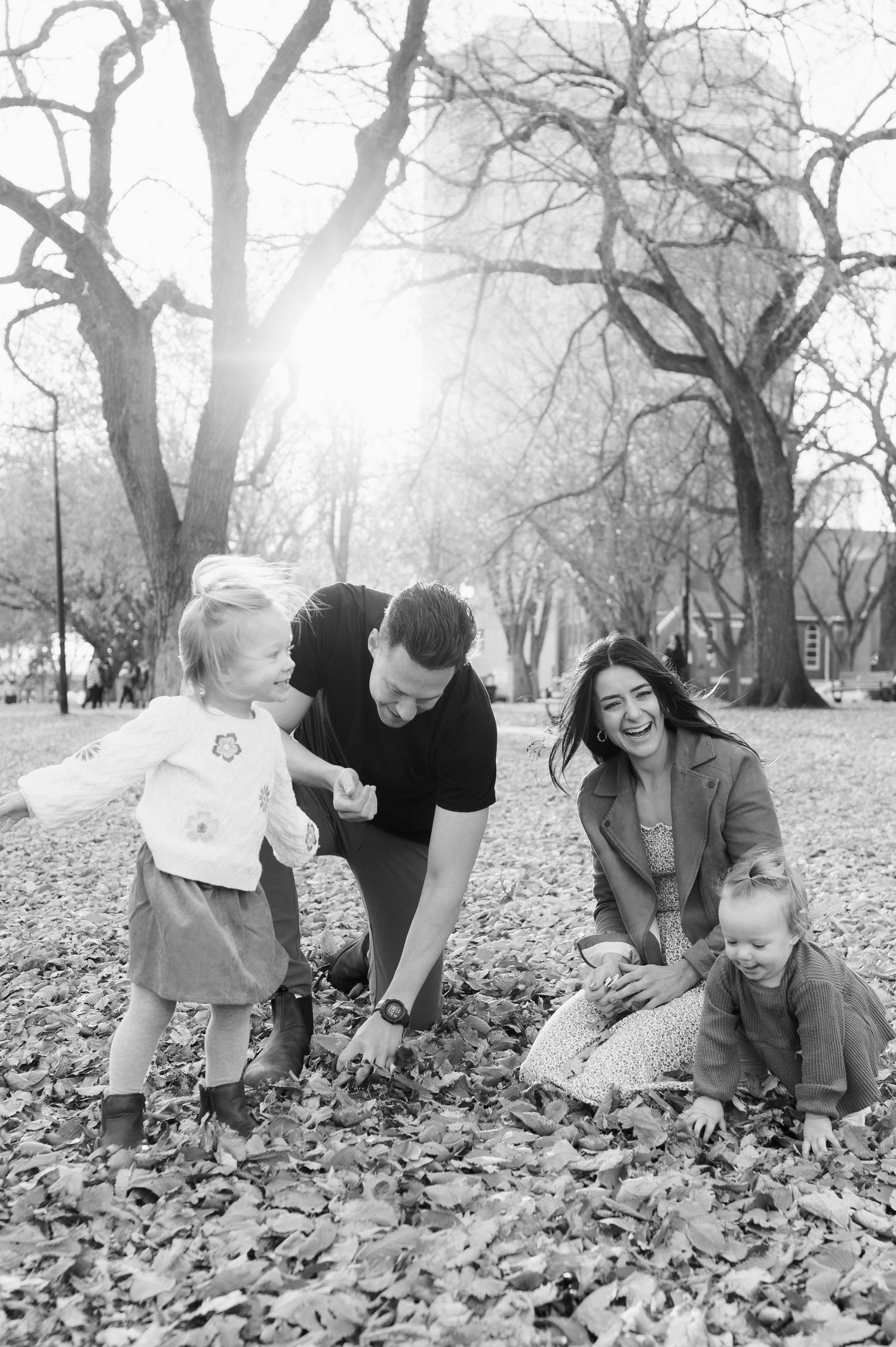 A black and white photo of a family playing in fallen autumn leaves.