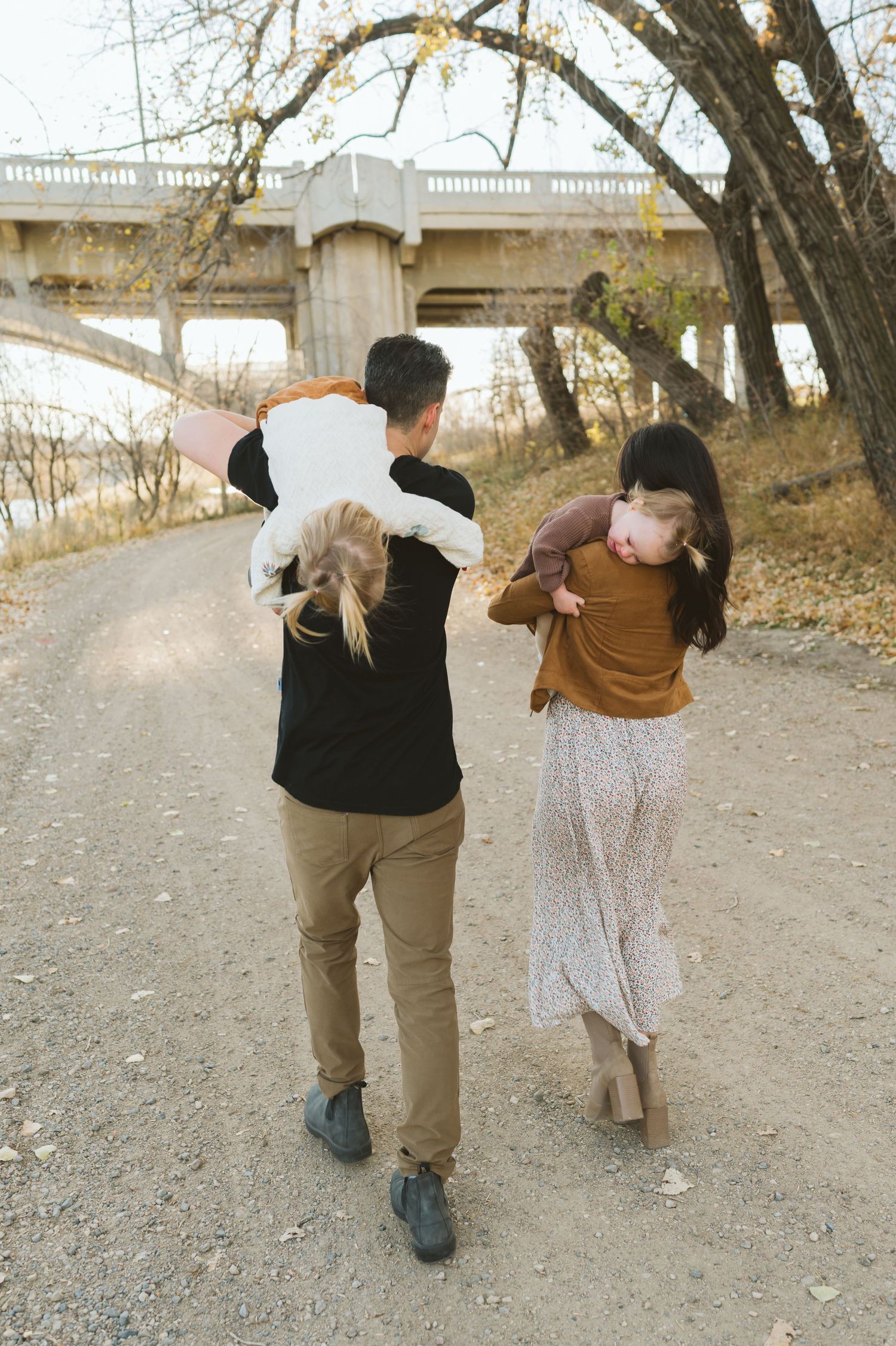 A couple walking together on a dirt path beneath a concrete bridge.